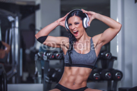 Fototapety Crazy fit girl posing in gym with headphone.