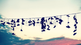 Fototapety Retro stylized silhouettes of shoes hanging on cable at sunset, teenage rebellion concept.