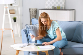 Beautiful young woman calculating taxes at home