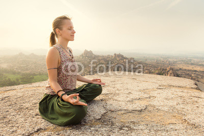 Young woman meditating at mountain cliff on sunrise