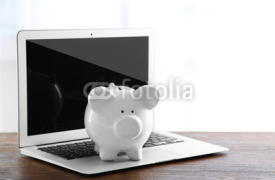 Obrazy i plakaty Piggy bank with laptop on wooden table indoors