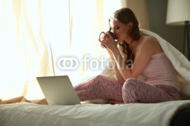 Young beautiful woman sitting in bed with laptop