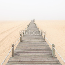 Naklejki Wooden footbridge on a foggy sand beach background. Portugal.
