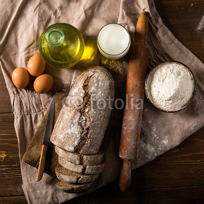 Still life photo of bread and flour with milk and eggs at the wo