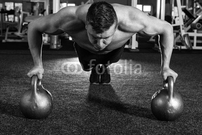 Handsome muscular man doing push ups on kettle ball